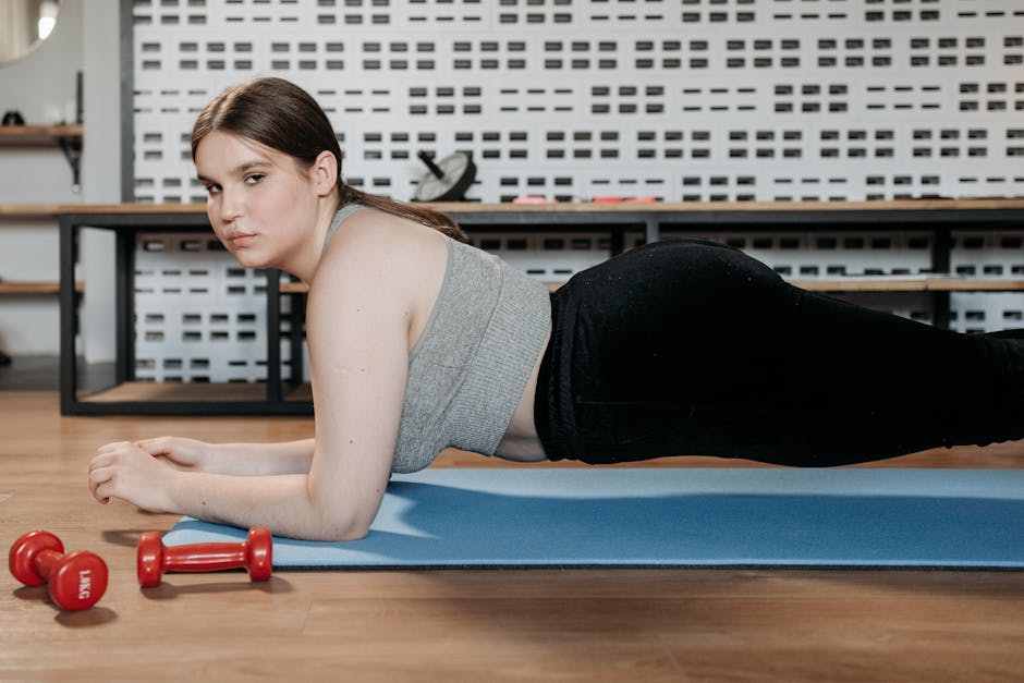 Woman doing planks on a yoga mat indoors with dumbbells showing dedication to fitness.