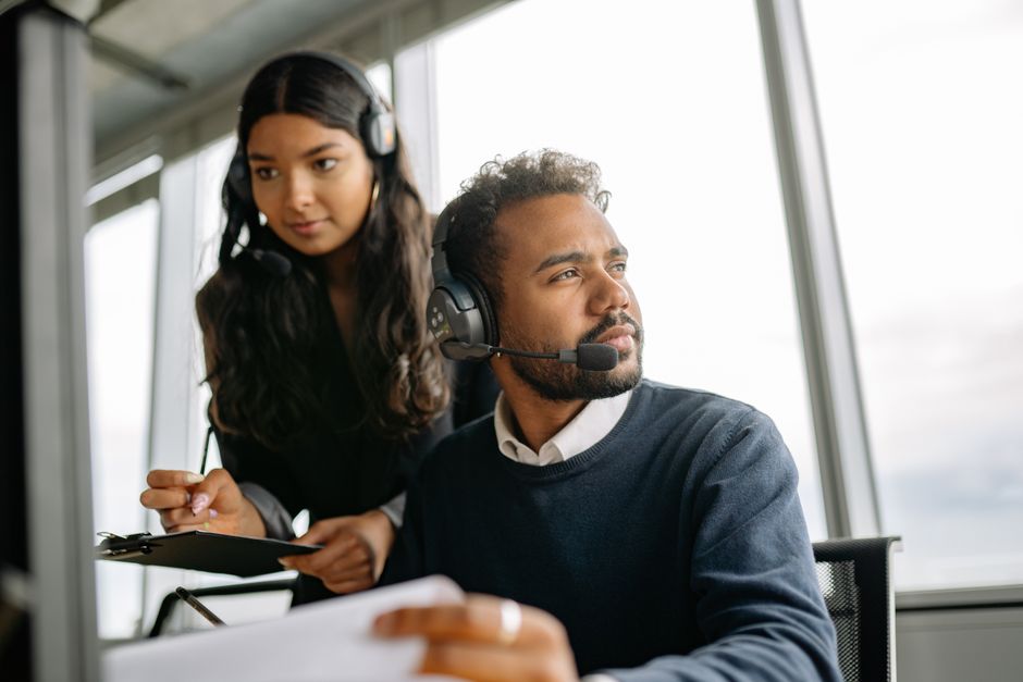 Dos profesionales trabajando con auriculares en una oficina moderna, enfocados en tareas de servicio.