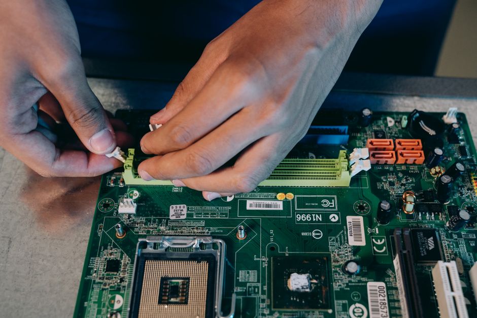 Manos ensamblando cuidadosamente una placa base de computadora, mostrando trabajo técnico en electrónica.