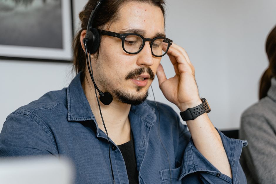 Hombre con barba y lentes trabajando con auriculares en un centro de soporte al cliente